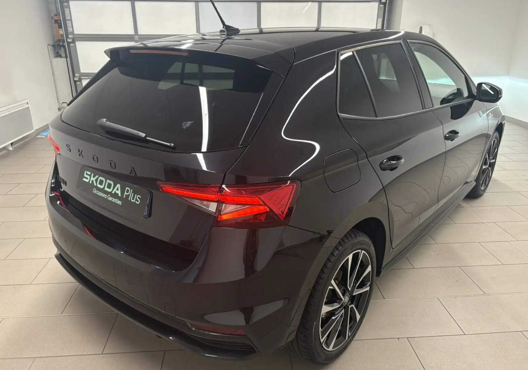 Vue 3/4 arrière droite d'une Skoda Fabia 2025 noire nacrée avec jantes alliage et feux arrière allumés en intérieur.