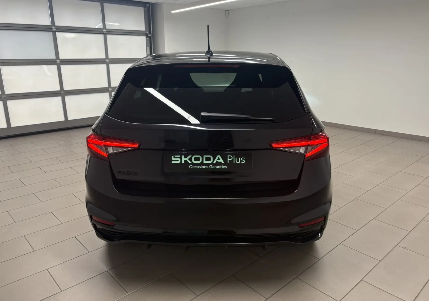 Vue arrière d'une Skoda Fabia 2025 noire nacrée, avec feux arrière allumés dans un garage lumineux.