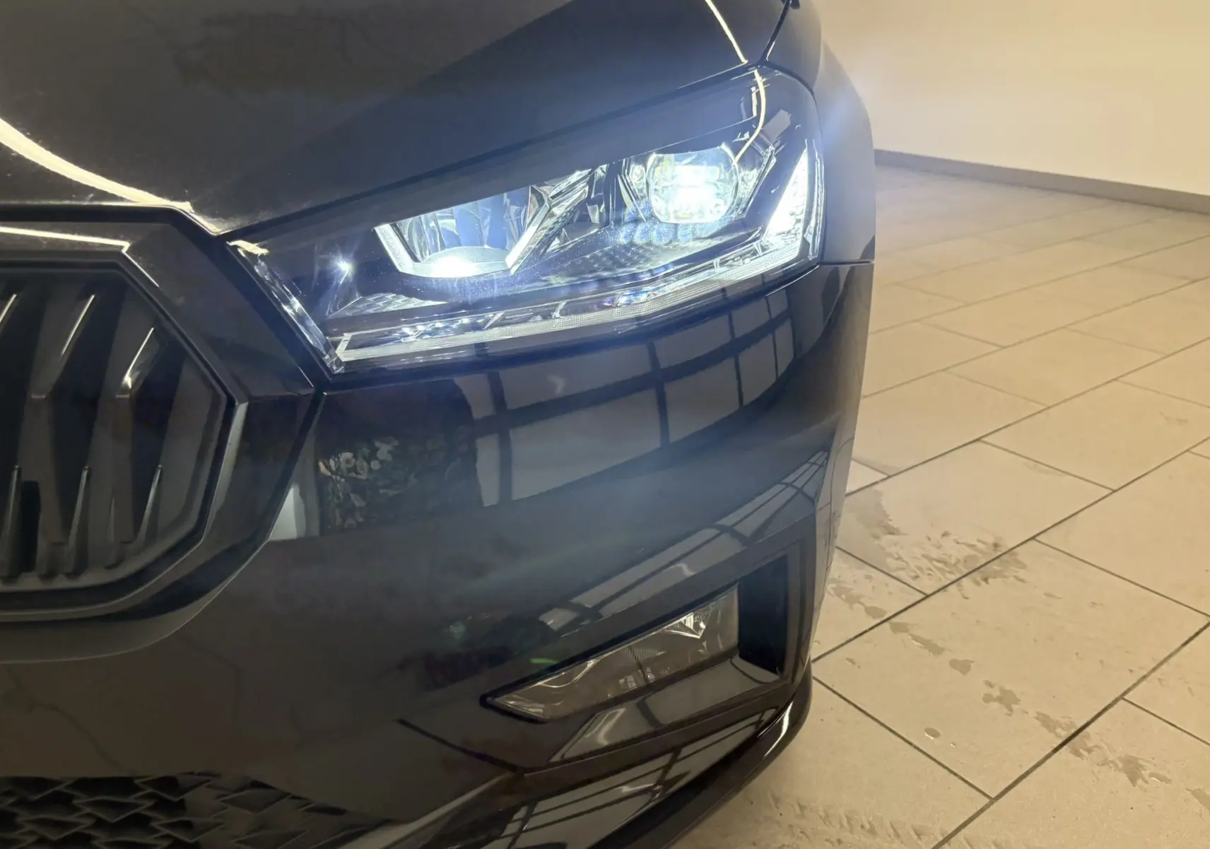 Gros plan sur le phare avant droit d'une Skoda Fabia 2025 noire nacrée avec calandre et feux allumés.