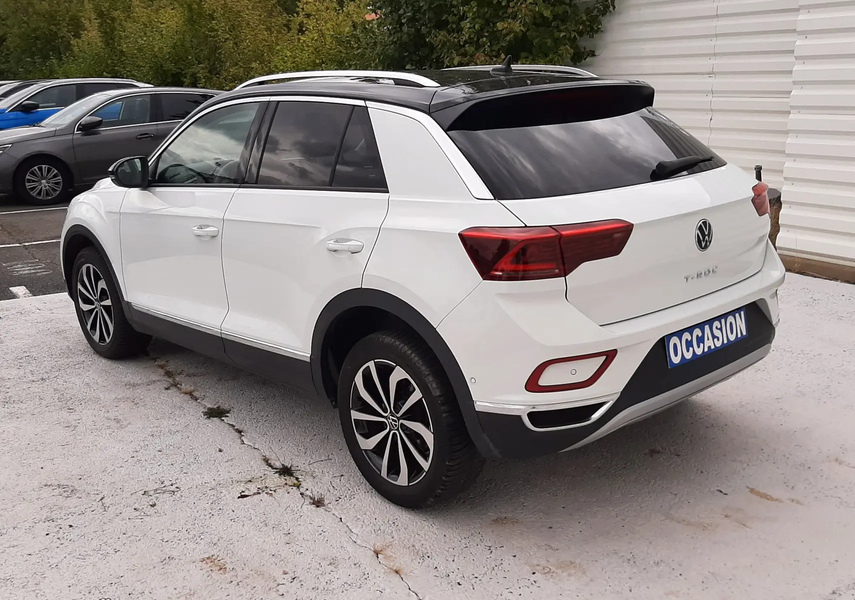 Volkswagen T-Roc blanc pur avec toit noir vu en 3/4 arrière droit sur parking extérieur.