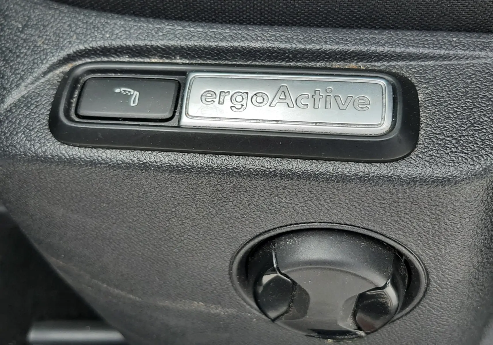 Détail du bouton ergoActive sur le côté du siège en tissu noir du Volkswagen T-Roc blanc toit noir.