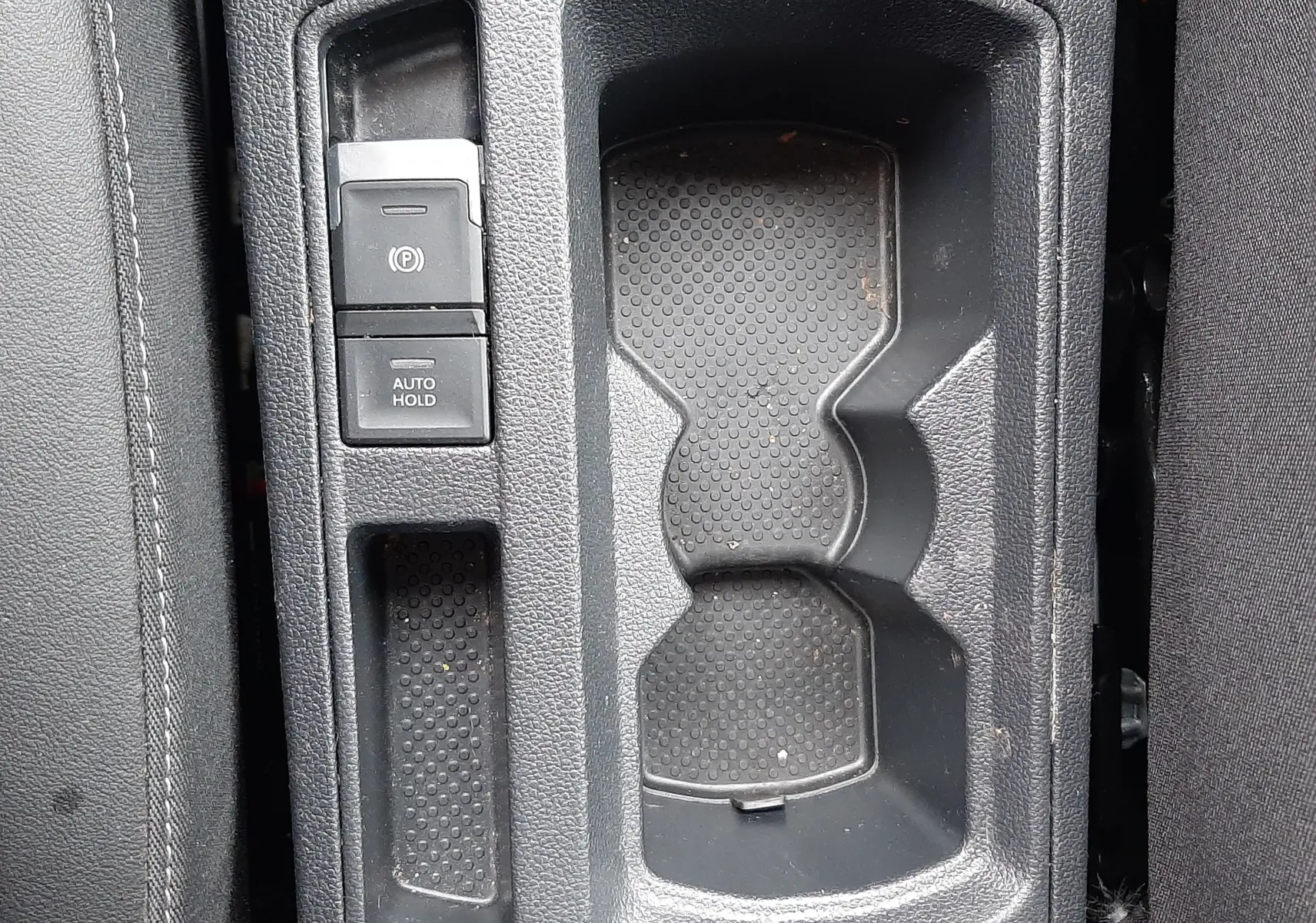 Vue plongeante sur la console centrale noire du Volkswagen T-Roc 2.0 TDI 150CH Style avec porte-gobelets et boutons de frein à main électronique.