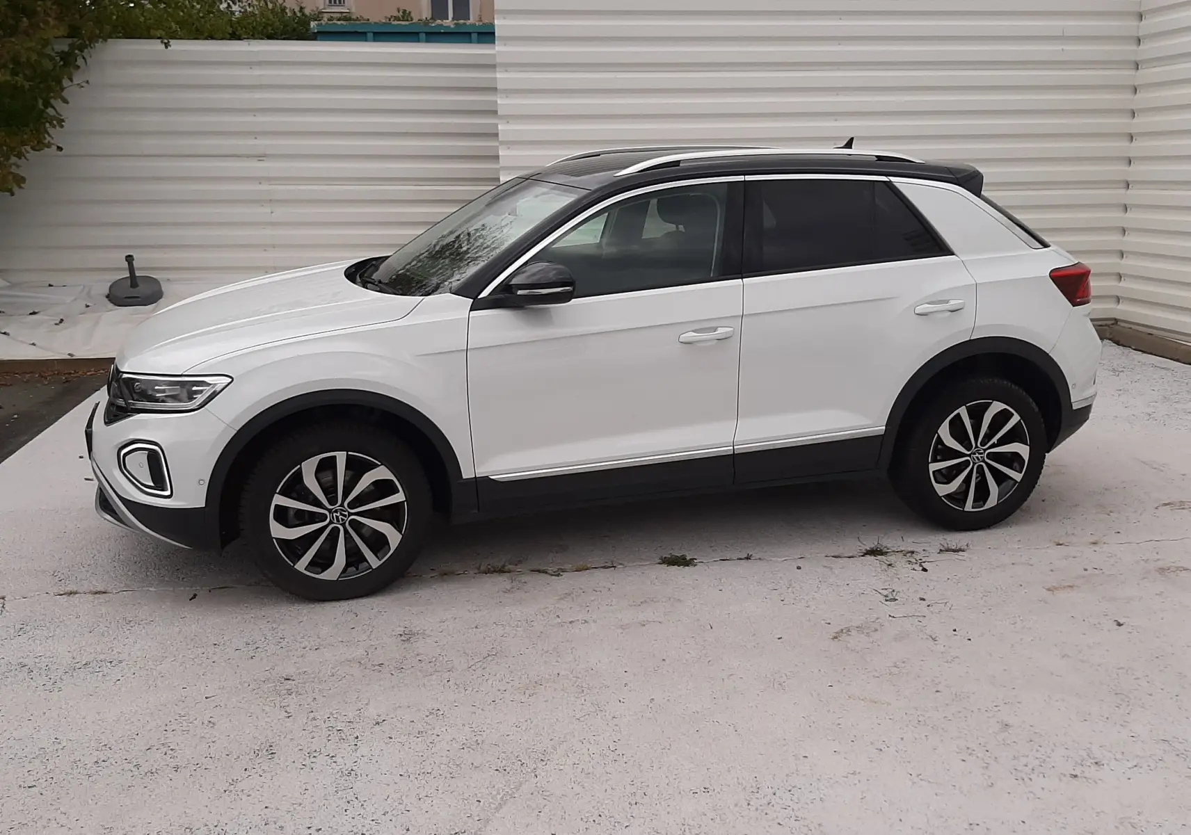 Vue de profil côté gauche d'un Volkswagen T-Roc blanc pur avec toit noir et jantes alliage bicolores.