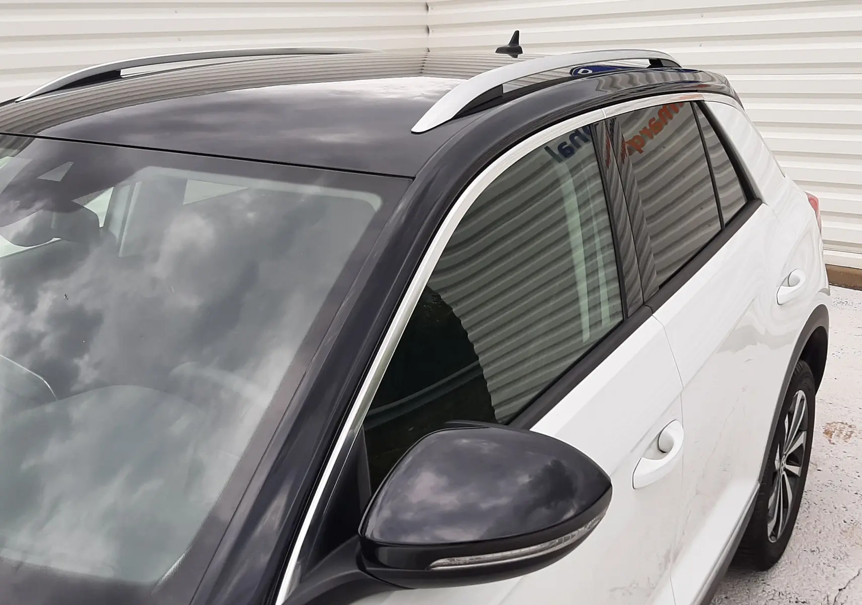 Vue 3/4 avant droit du Volkswagen T-Roc blanc pur avec toit noir brillant et rétroviseur assorti.