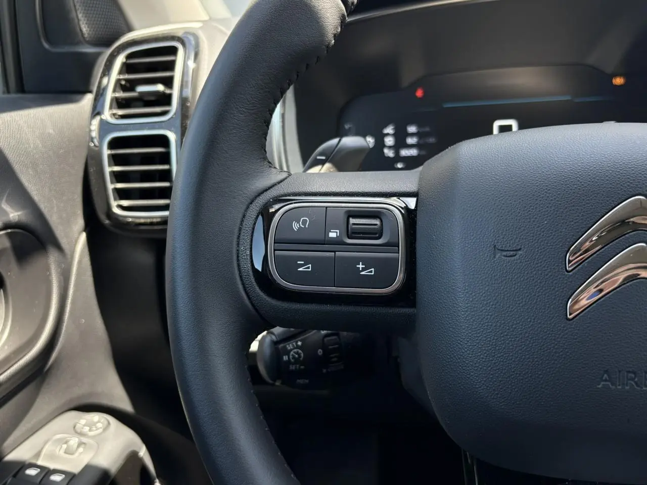 Gros plan sur le volant noir du Citroën C5 Aircross Hybrid 2025, avec commandes intégrées et aérateurs chromés à gauche.