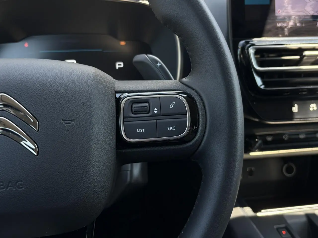 Gros plan sur le volant en cuir noir du Citroën C5 Aircross Hybrid 2025, avec commandes intégrées et tableau de bord partiel visible.