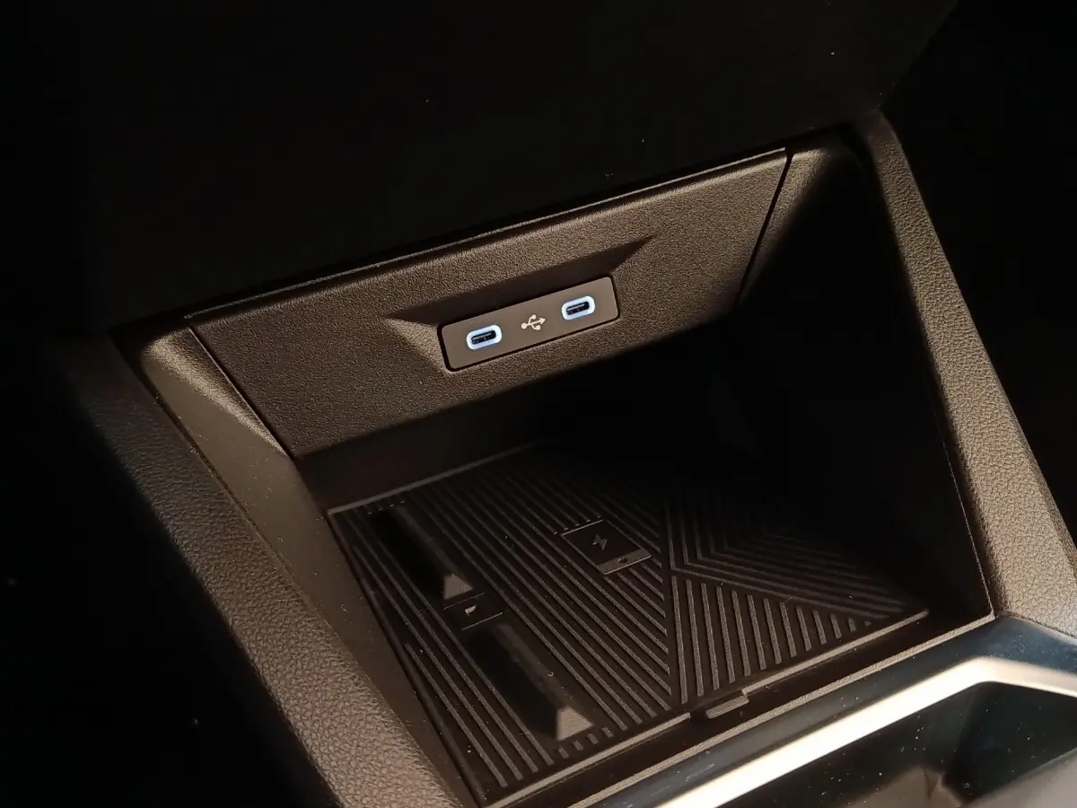 Gros plan sur la console centrale de la Renault Clio Techno gris foncé, montrant les ports USB-C et le chargeur sans fil.