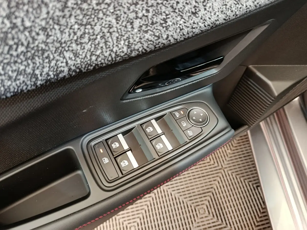 Gros plan sur la commande des vitres électriques côté conducteur d'une Renault Clio gris foncé, avec surpiqûres rouges.