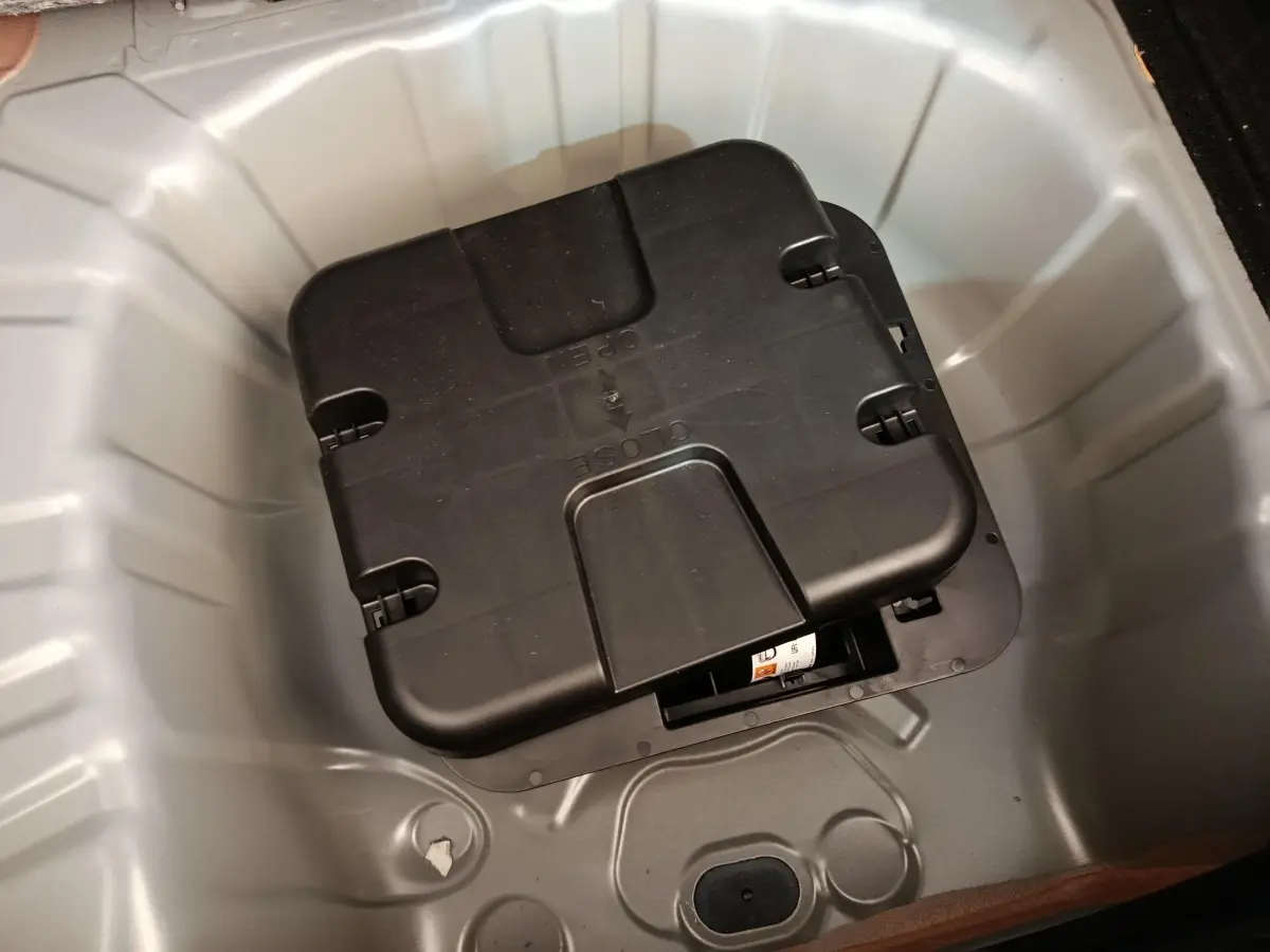 Coffre ouvert en vue plongeante montrant le rangement gris clair sous la tablette avec un boîtier noir au centre.