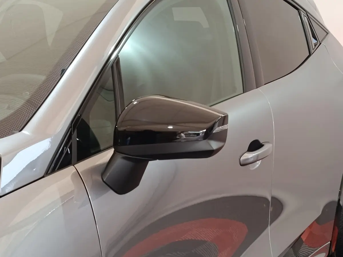 Vue rapprochée du côté gauche d'une Renault Clio Techno gris foncé, mettant en valeur le rétroviseur noir brillant et la poignée de porte.