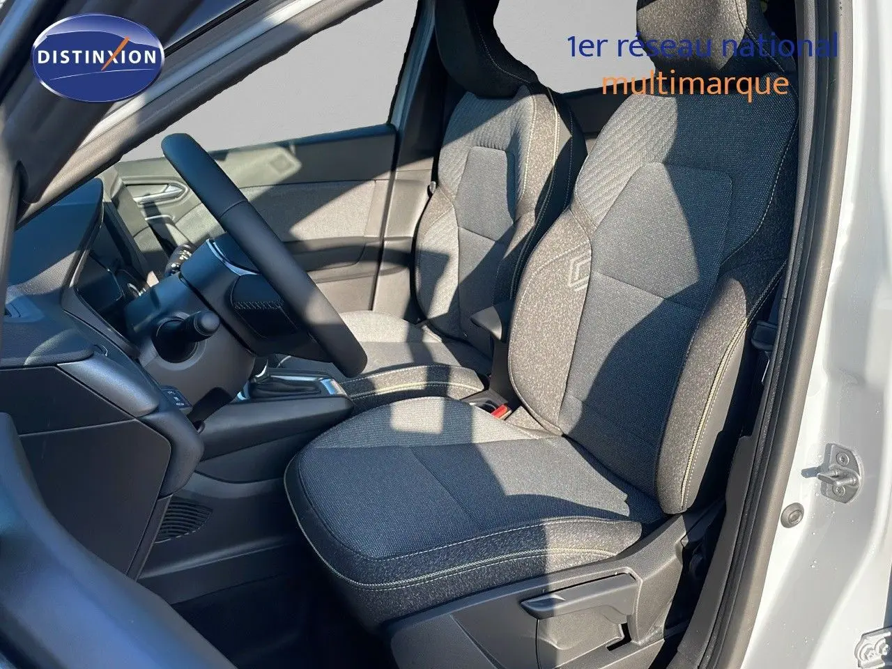 Intérieur avant droit du Renault Captur E-Tech 2025 avec sièges tissu gris et volant noir visible au soleil.