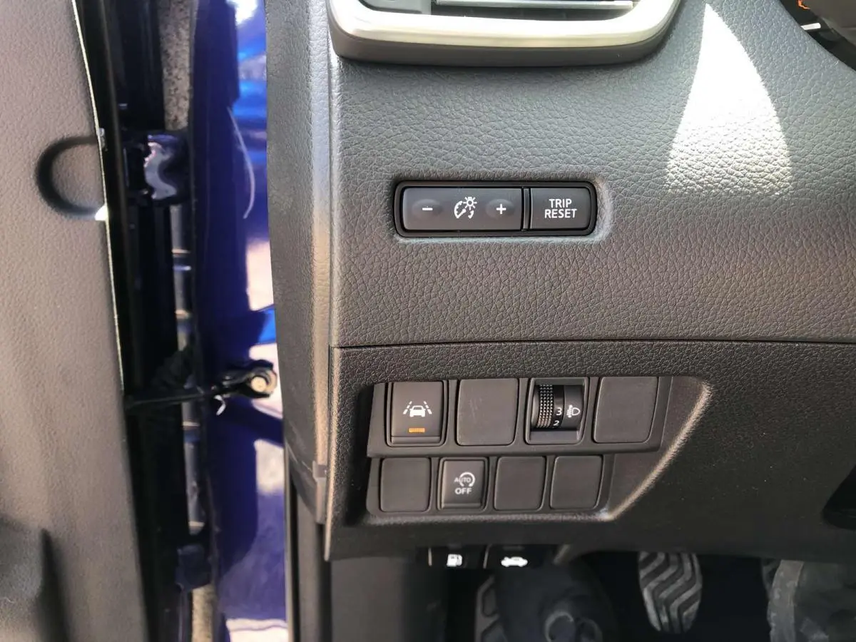 Vue rapprochée du tableau de bord côté gauche d'un Nissan Qashqai bleu, montrant les commandes d'éclairage et d'aide à la conduite.