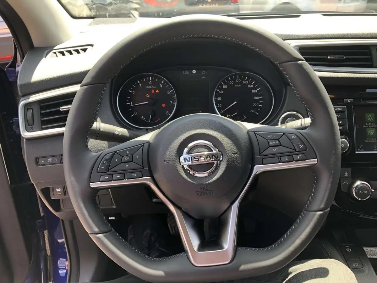 Vue centrée sur le volant cuir du Nissan Qashqai bleu, avec commandes intégrées et tableau de bord visible.