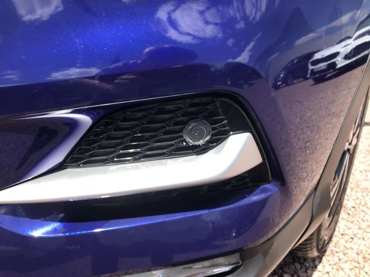 Gros plan sur la calandre avant droite du Nissan Qashqai 2019 bleu Topaze avec caméra de vision 360° intégrée.
