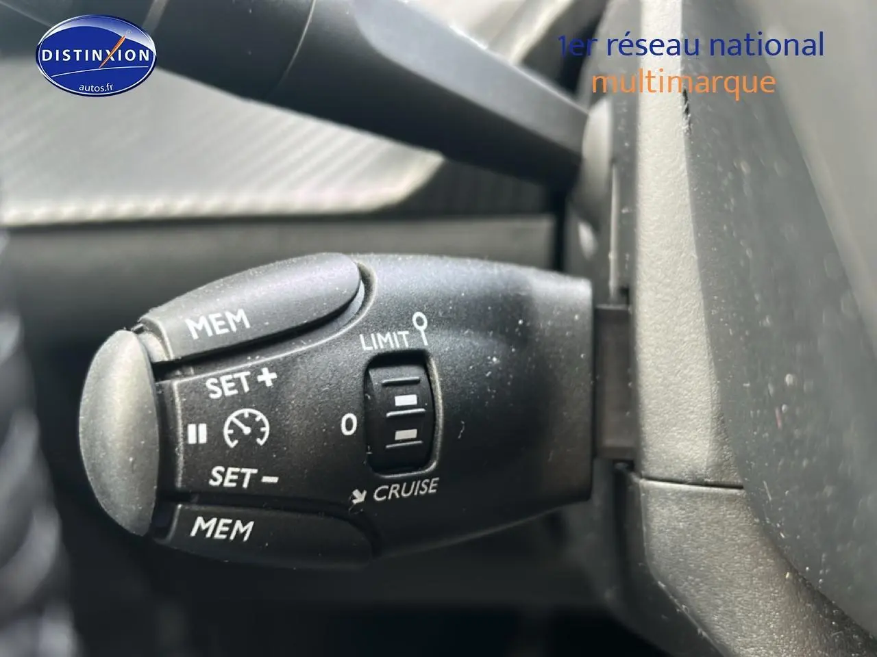 Gros plan sur la commande de régulateur de vitesse noire à gauche du volant dans une Peugeot 208 gris artense.