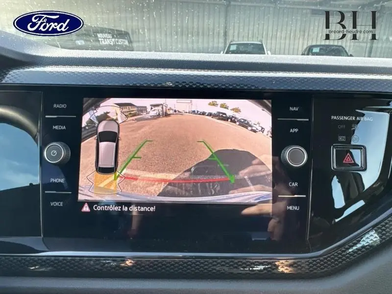 Écran tactile intérieur montrant la caméra de recul d'un Volkswagen Taigo blanc, avec guidage de trajectoire visible.