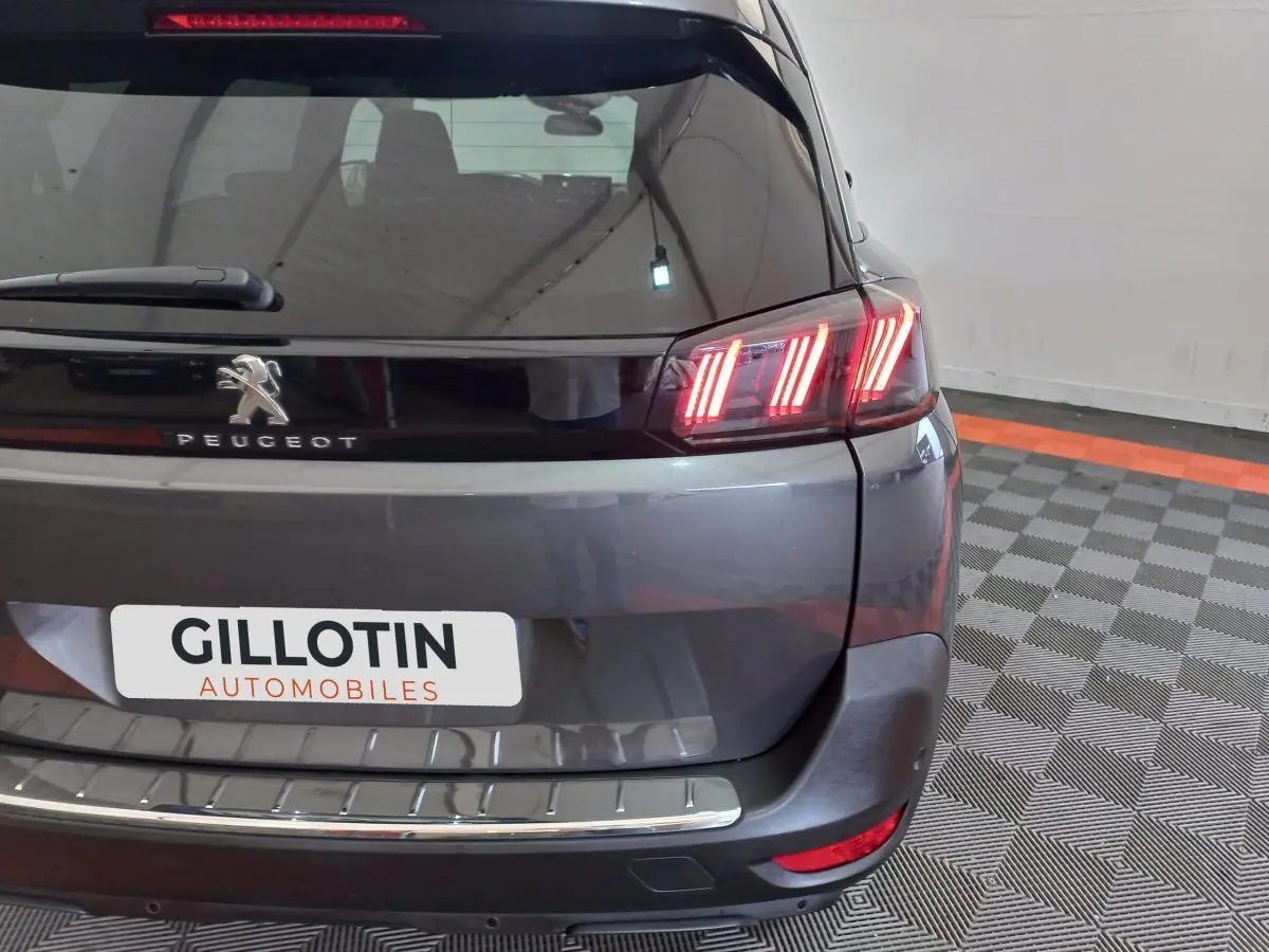 Vue arrière du Peugeot 5008 gris foncé avec feux arrière allumés et logo Peugeot bien visible.