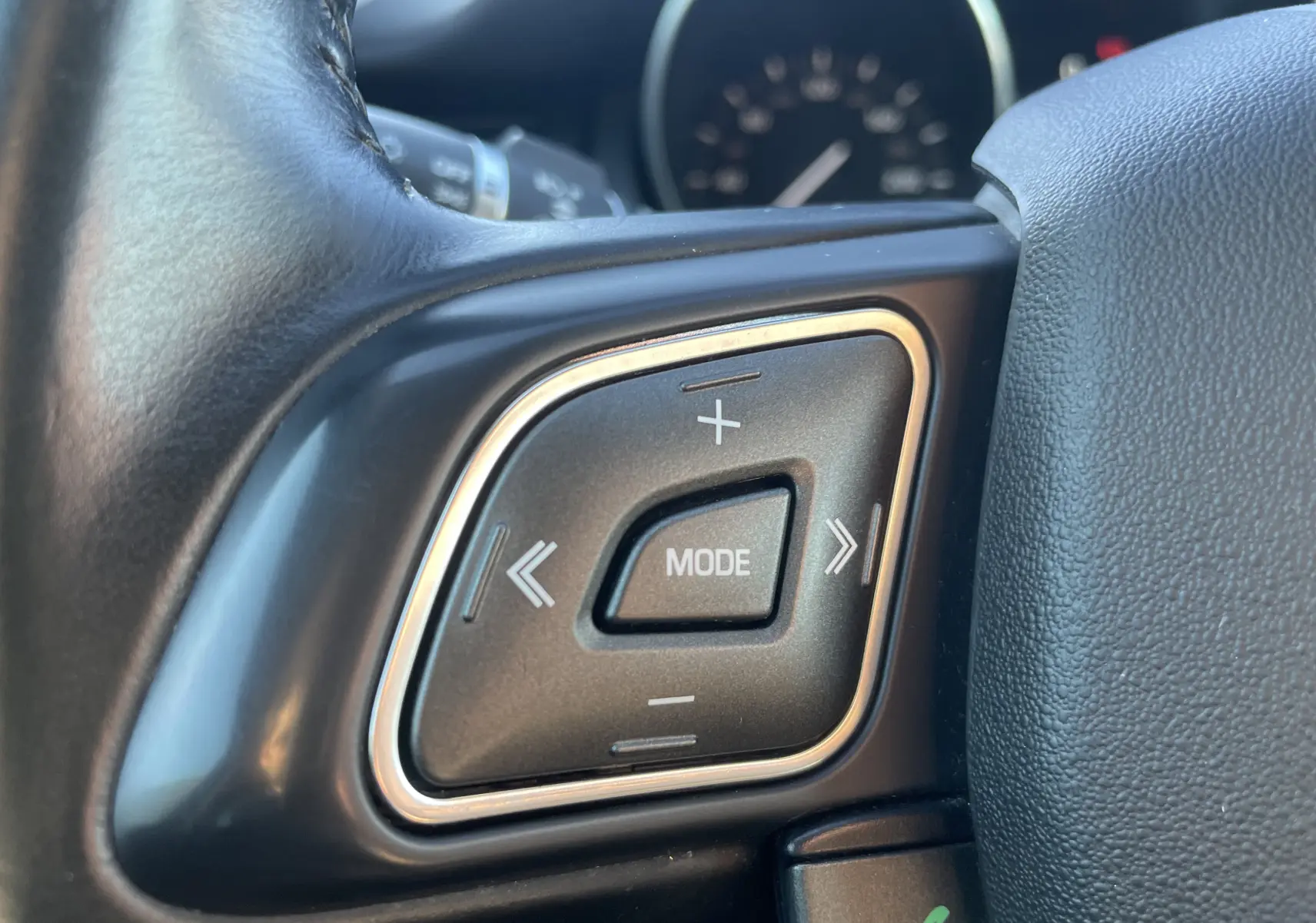 Gros plan sur les commandes multimédia au volant noir du Range Rover Evoque 2016, bouton central "MODE" entouré de touches + et -