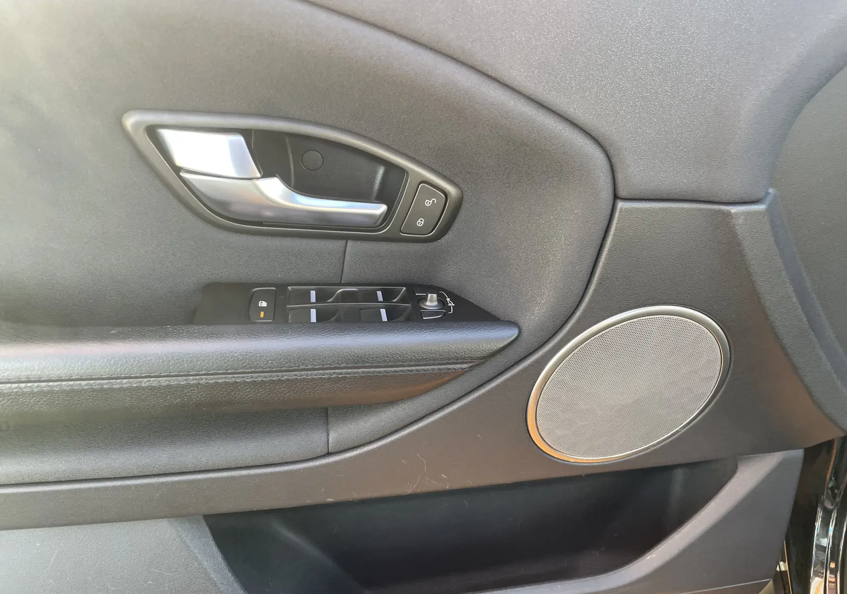 Gros plan sur la porte intérieure côté gauche du Range Rover Evoque noir, avec poignée argentée et commandes de vitres.