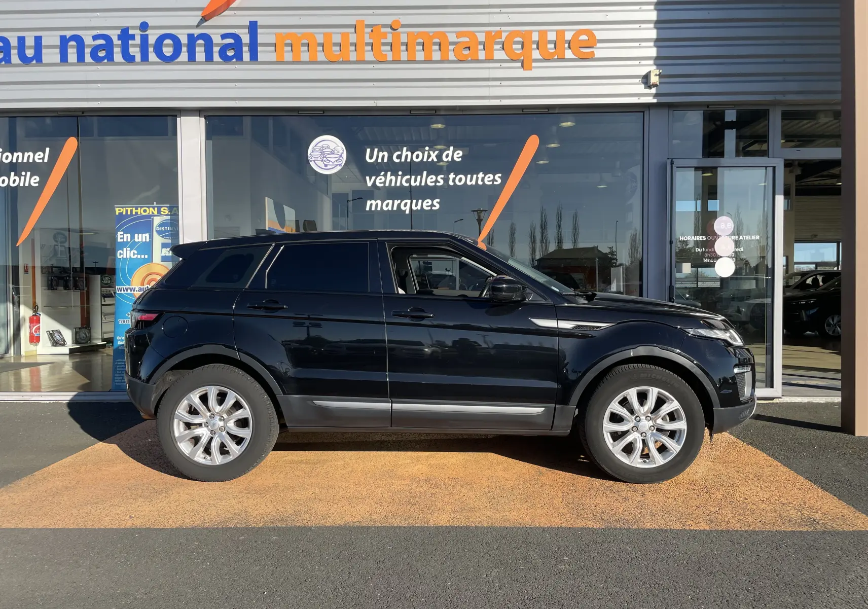 Vue de profil côté gauche d'un Range Rover Evoque noir 5 portes, avec jantes alliage et vitres teintées, devant un showroom.