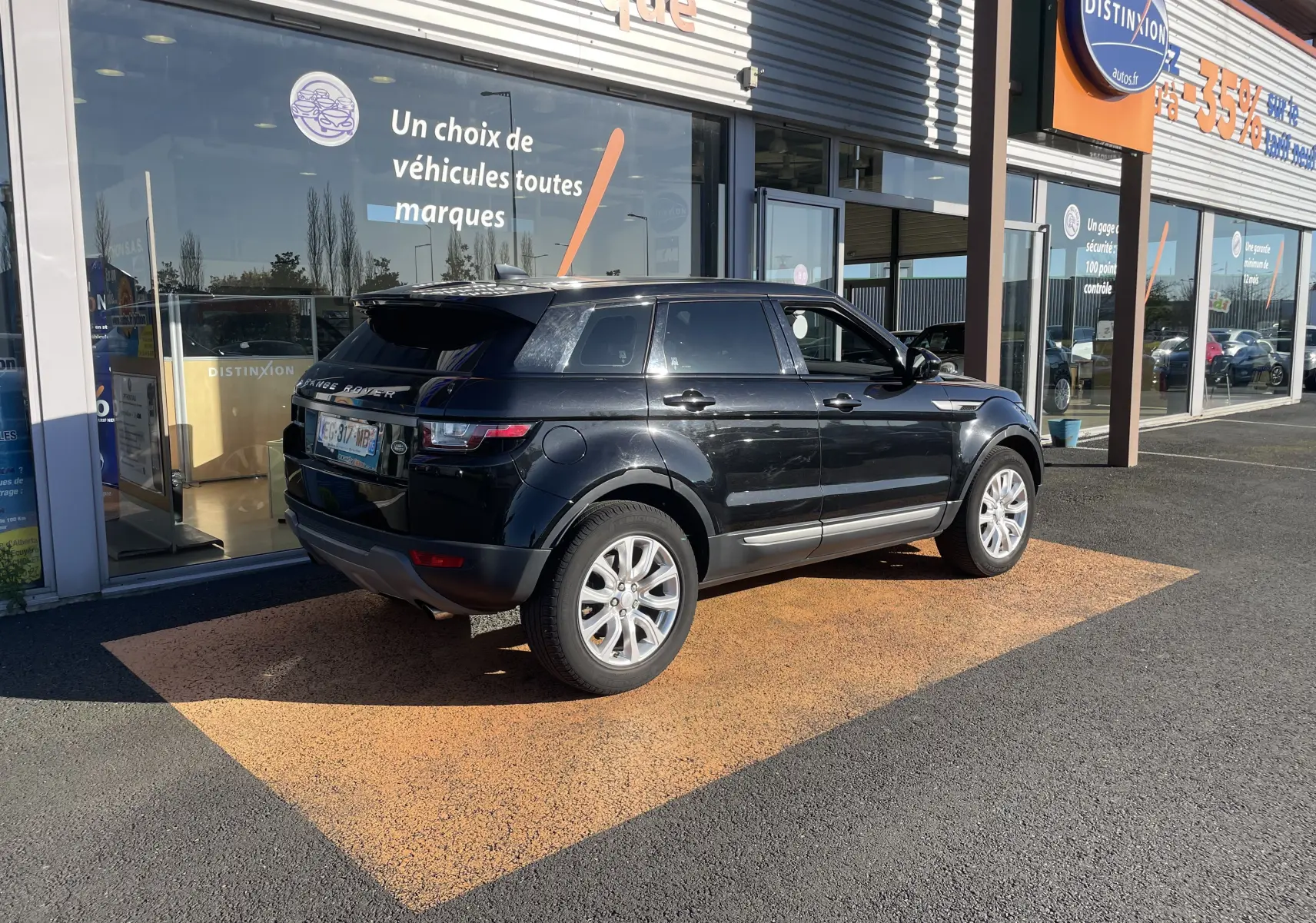 Vue 3/4 arrière droite d'un Range Rover Evoque noir 2016 garé devant une vitrine de concession.