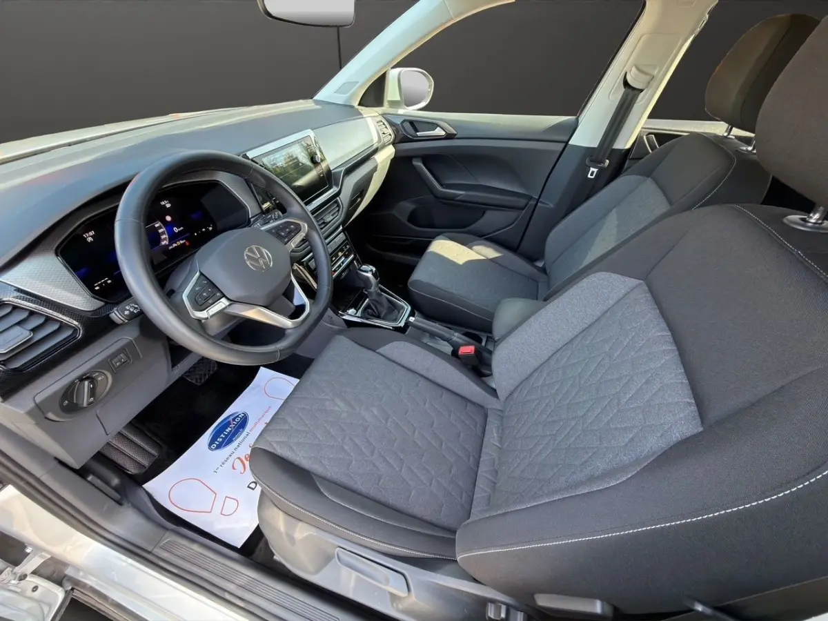 Vue intérieure côté conducteur du Volkswagen T-Cross 2025, montrant le volant cuir, tableau de bord numérique et sièges tissu gris.