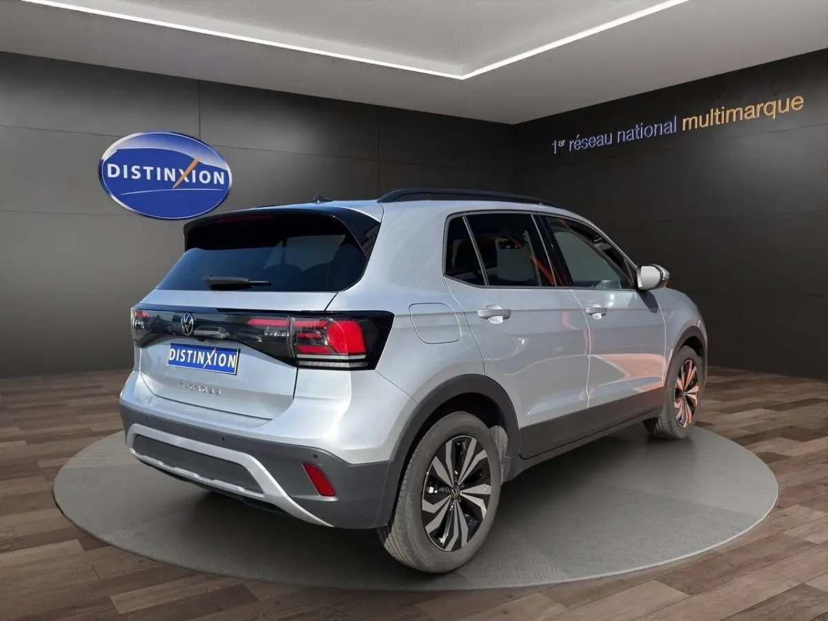 Vue 3/4 arrière droite du Volkswagen T-Cross gris clair 2025 avec jantes alliage et toit noir en showroom.