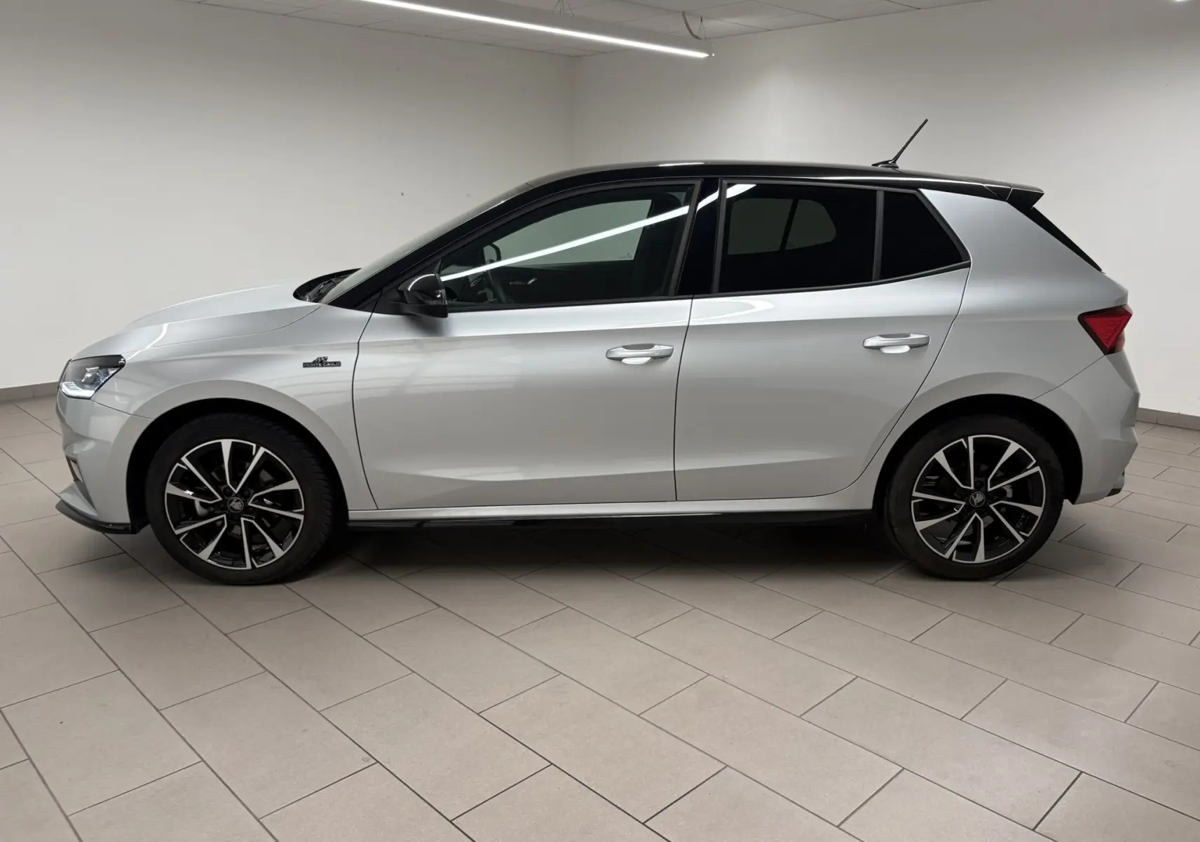 Vue de profil côté gauche d'une Skoda Fabia 2025 gris argent avec toit noir et jantes noires à motifs argentés.