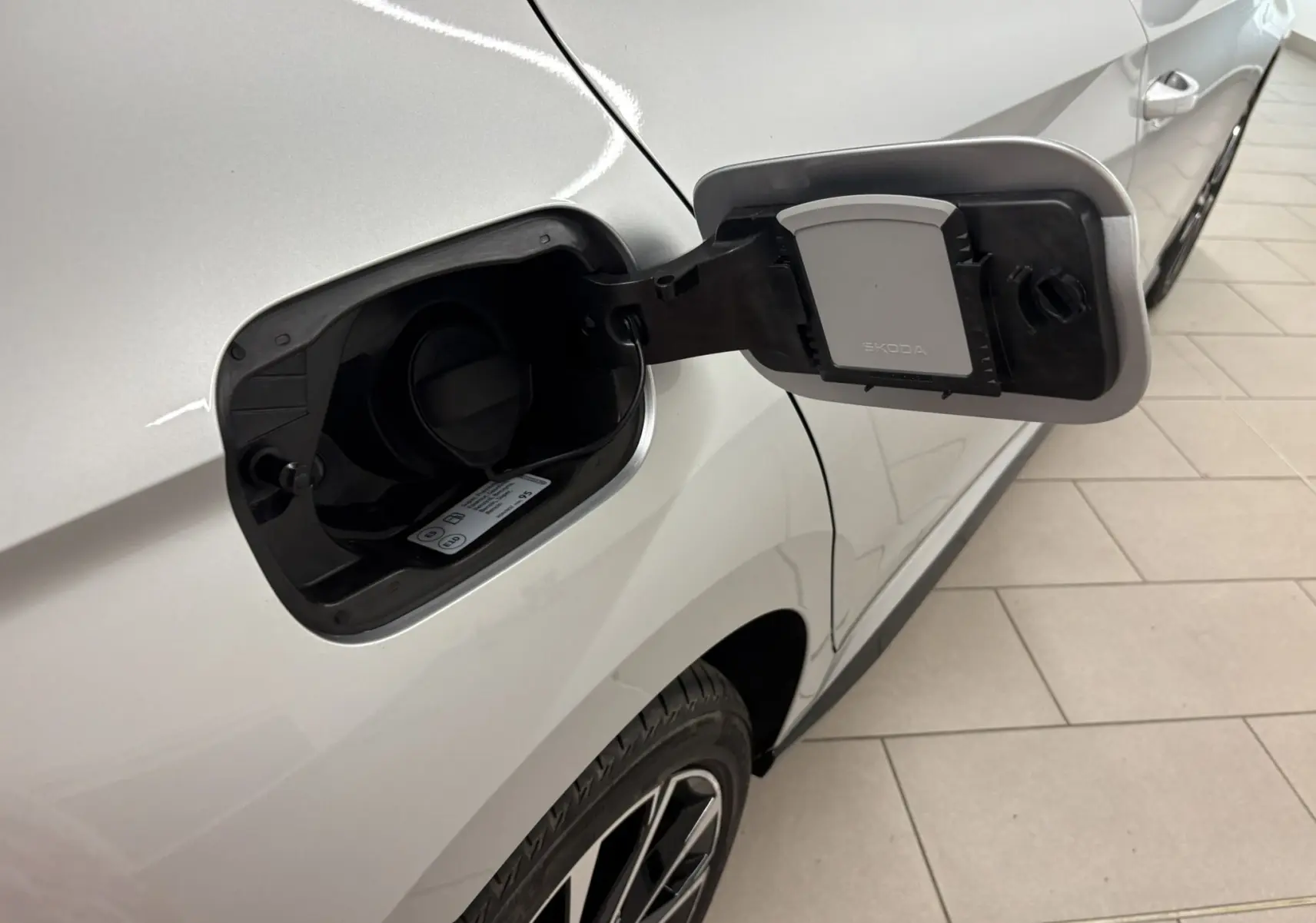 Gros plan sur la trappe à carburant ouverte côté gauche d'une Skoda Fabia gris argent avec toit noir, vue partielle de la roue arrière.
