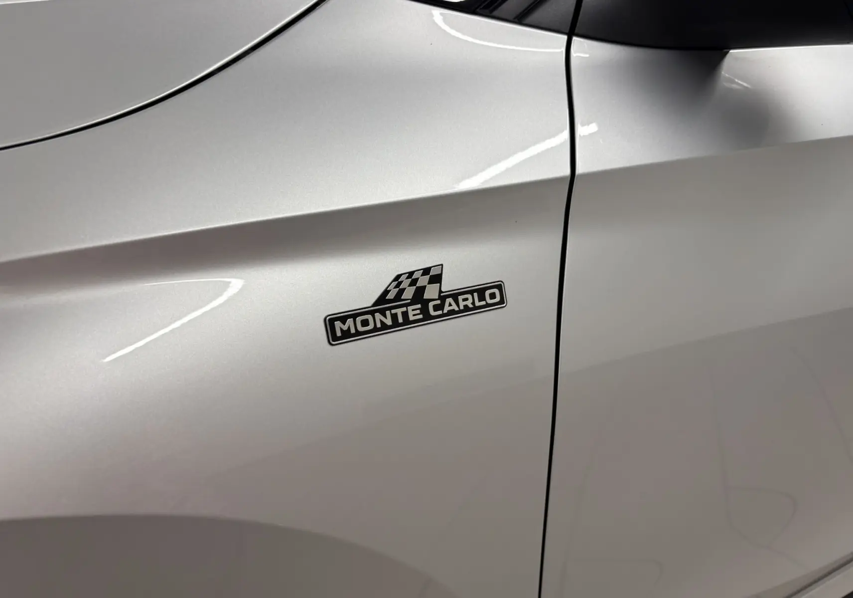 Gros plan sur l'aile avant gauche gris argent d'une Skoda Fabia Monte Carlo avec logo distinctif noir et damier.