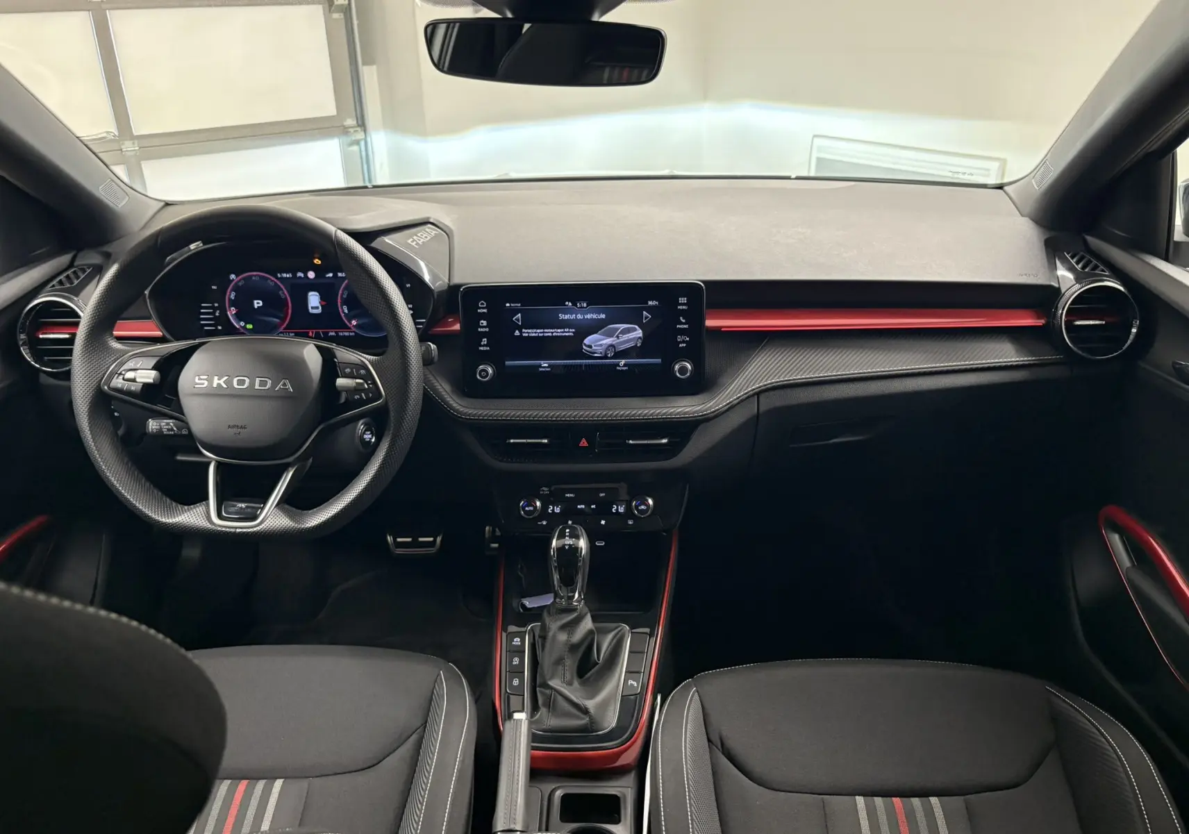 Intérieur de la Skoda Fabia 2025 vue de face, tableau de bord noir avec touches rouges et écran tactile central.