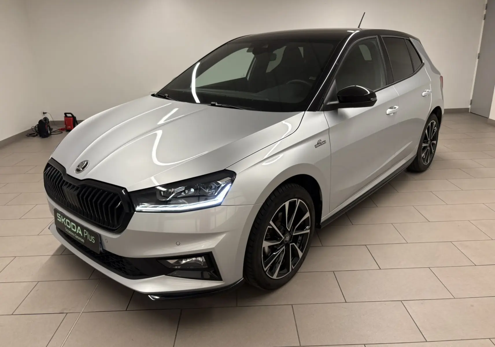 Vue 3/4 avant droite d'une Skoda Fabia 2025 gris argent avec toit noir et jantes noires distinctives en intérieur.