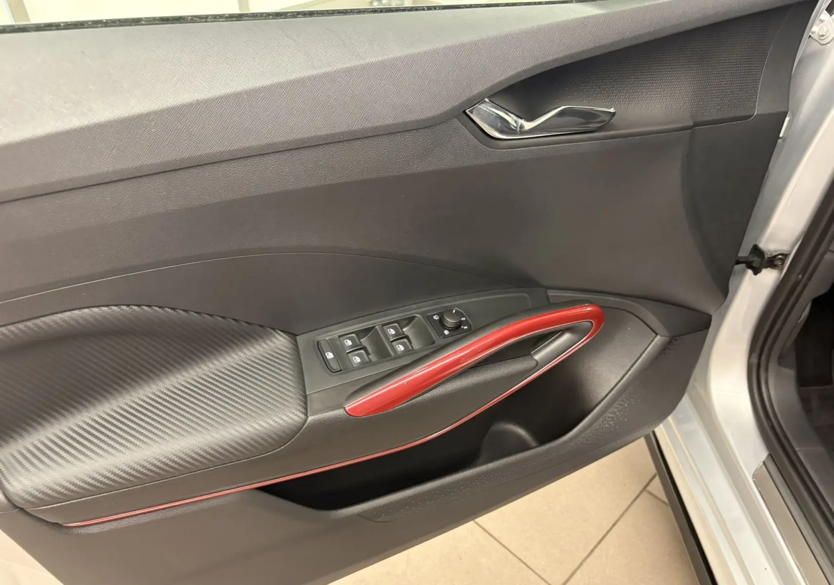 Vue intérieure côté gauche de la porte avant d'une Skoda Fabia 2025 gris argent avec poignée rouge et commandes électriques.