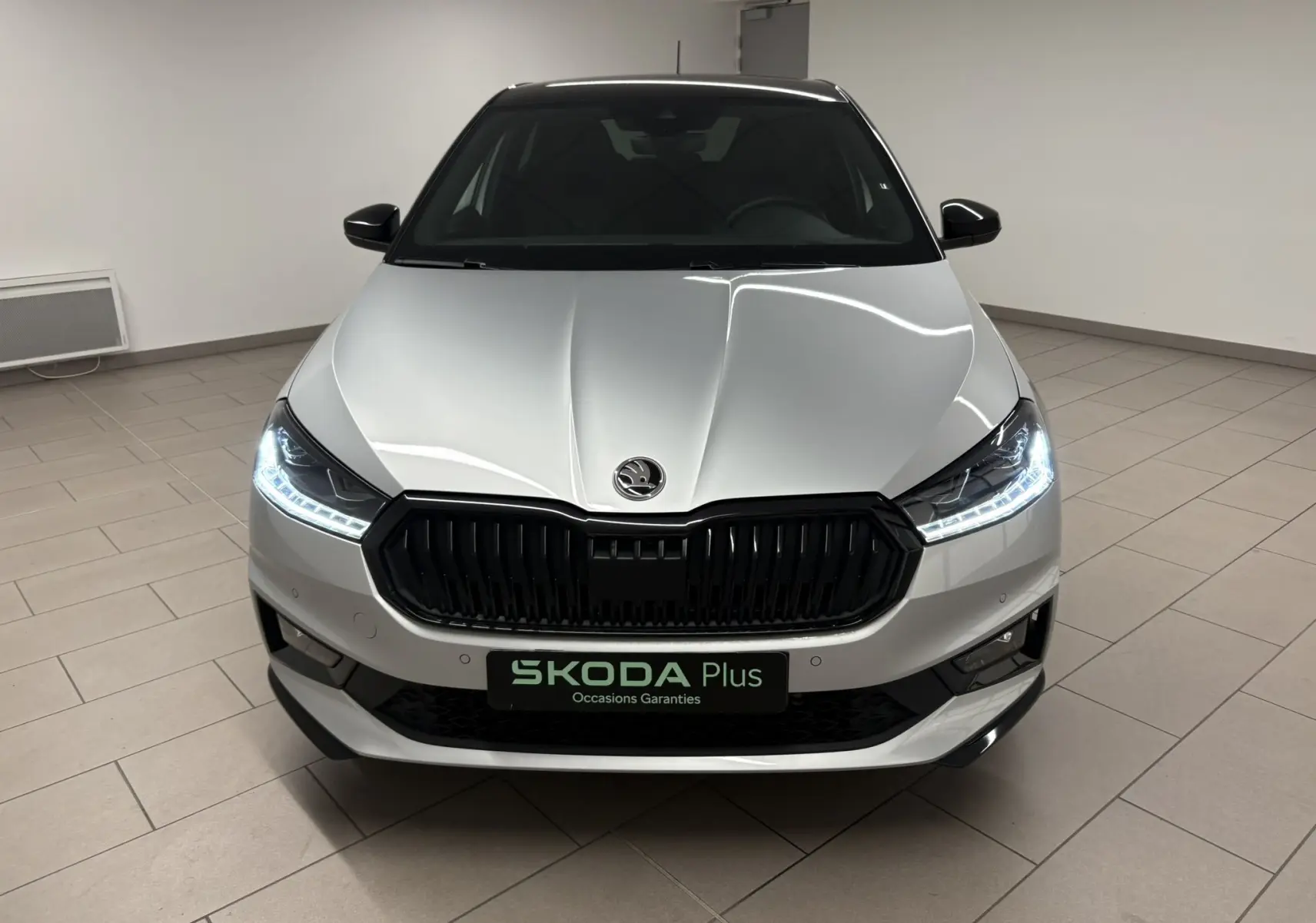 Vue frontale d'une Skoda Fabia 2025 gris argent avec toit noir, phares LED allumés dans un showroom.