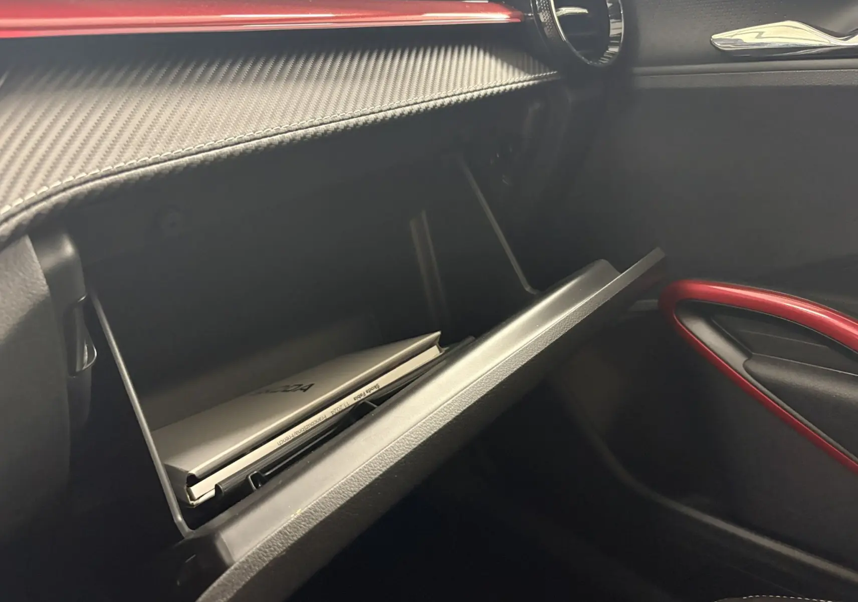 Gros plan sur la boîte à gants ouverte de la Skoda Fabia Monte Carlo 2025, avec garniture intérieure noire et détails rouges.