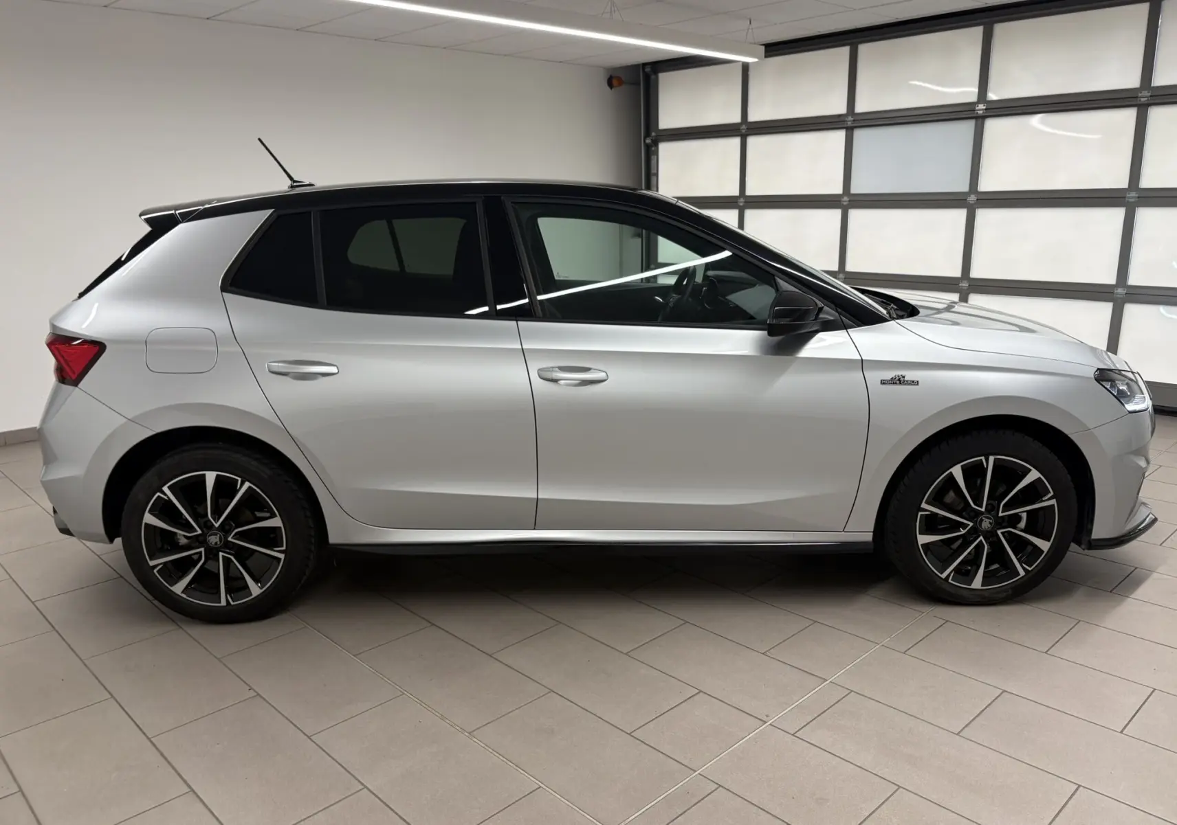 Vue de profil côté gauche d'une Skoda Fabia 2025 gris argent avec toit noir et jantes noires à motifs argentés.