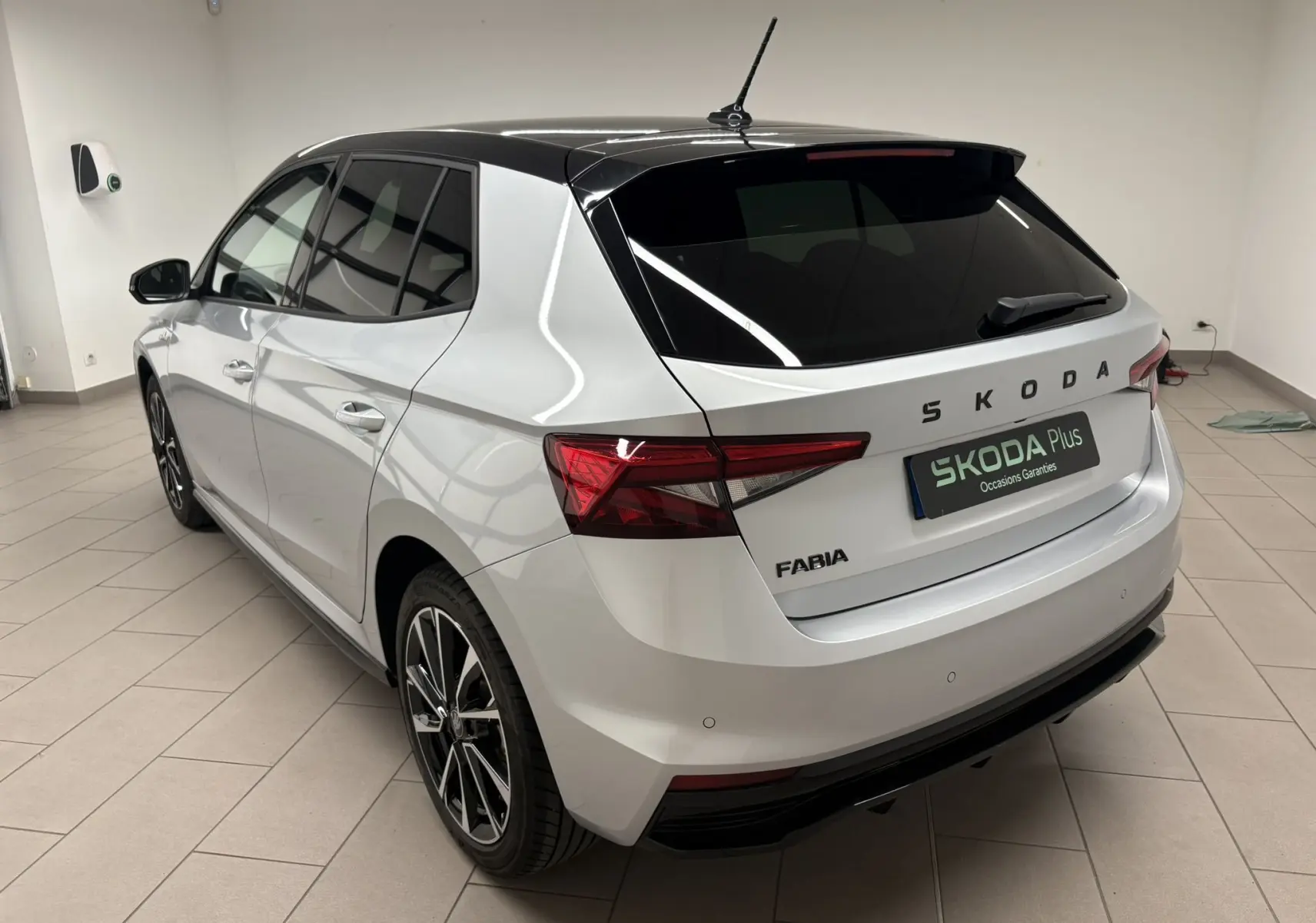 Vue 3/4 arrière droite d'une Skoda Fabia 2025 gris argent avec toit noir et jantes alliage noires en intérieur showroom.
