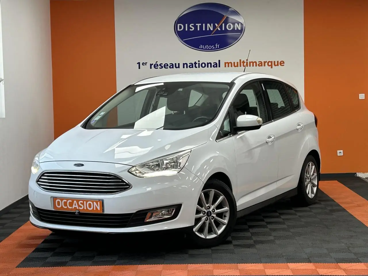 Ford C-MAX blanc en 3/4 avant droit, avec calandre chromée et jantes alliage 16 pouces dans un showroom.