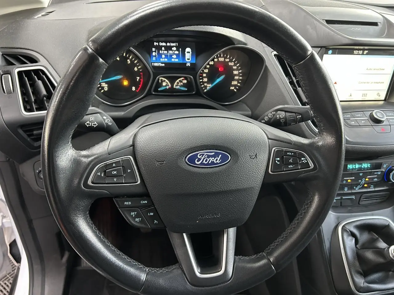 Vue rapprochée du volant noir Ford C-MAX 2018 avec tableau de bord et écran tactile SYNC 3 en arrière-plan.