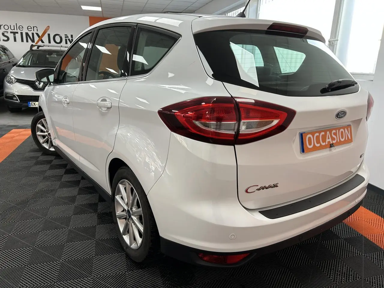 Vue 3/4 arrière droite d'une Ford C-MAX blanche 2018 en showroom avec plaque "OCCASION" visible.