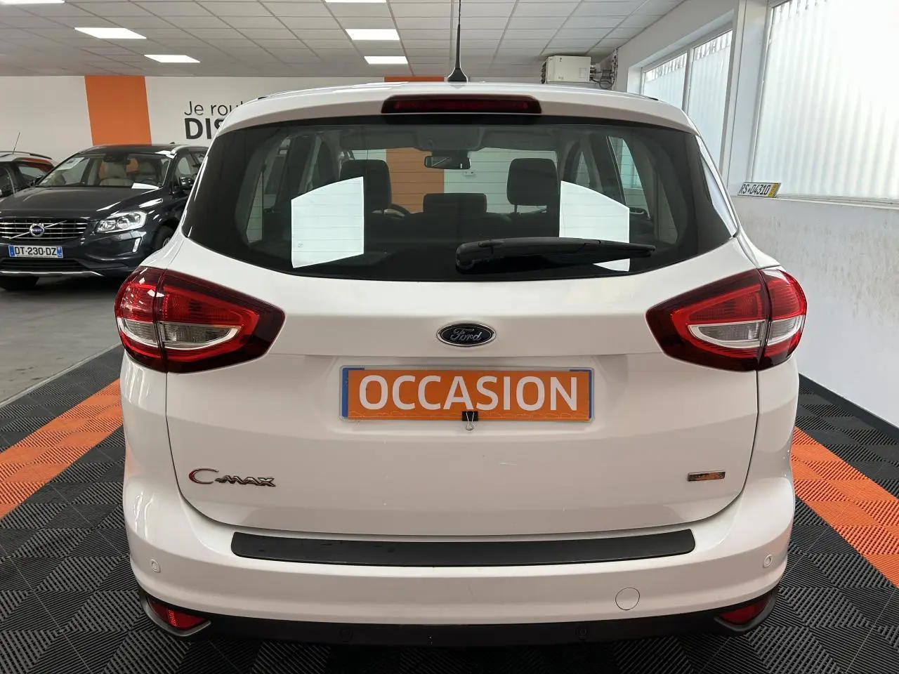 Vue arrière d'un Ford C-MAX blanc 2018 avec logo, feux rouges et plaque "OCCASION" en intérieur showroom.