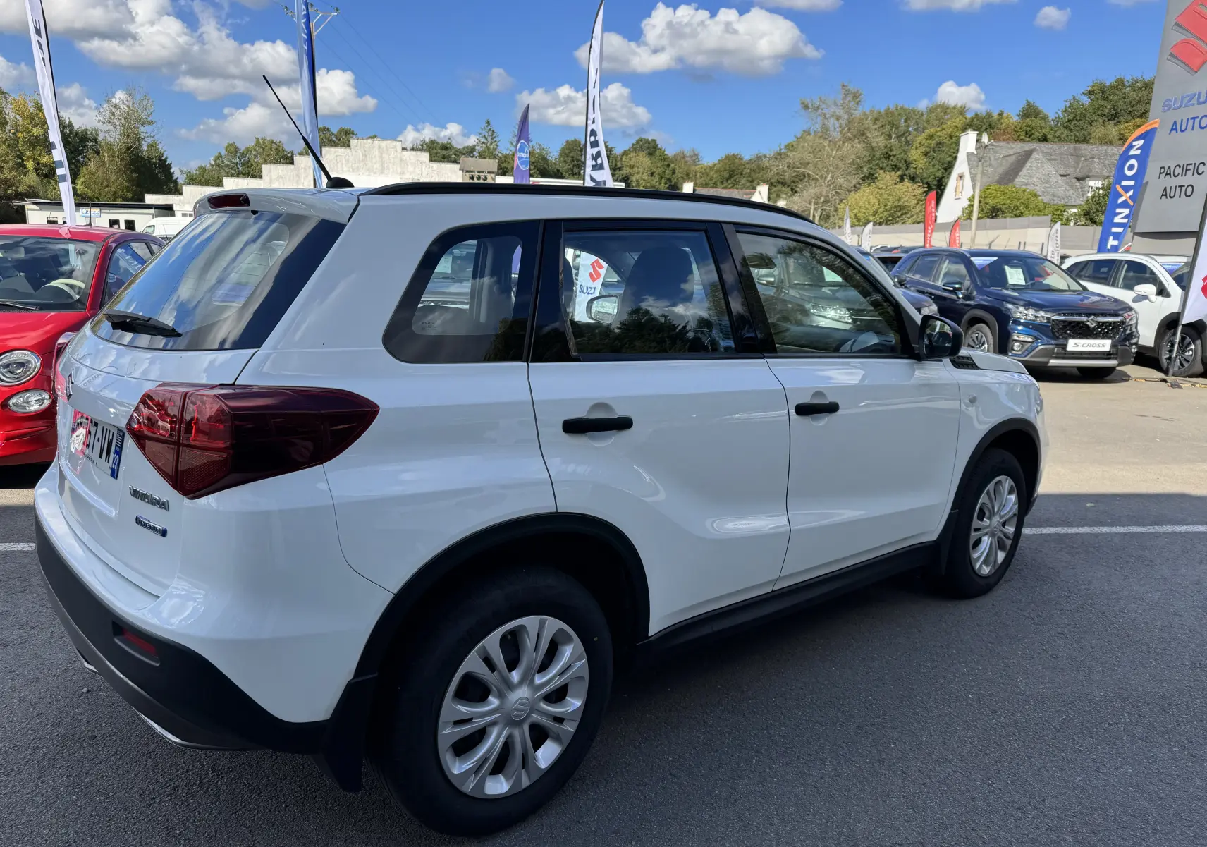 Vue 3/4 arrière droite d'un Suzuki Vitara blanc 2023 hybride essence à cinq portes sur un parking extérieur.