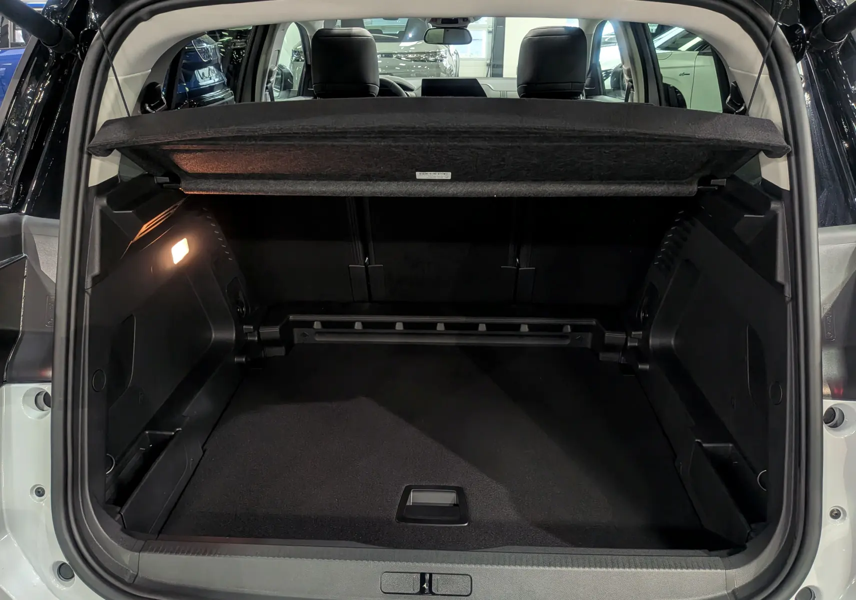 Coffre ouvert du Citroën C5 Aircross hybride blanc Okénite avec toit noir, vue arrière montrant l’espace de chargement et la tablette cache-bagages.