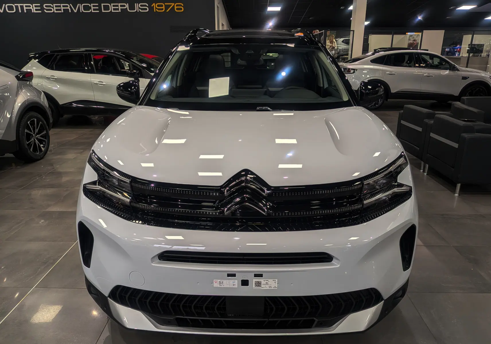 Vue de face du Citroën C5 Aircross hybride blanc Okénite avec toit noir brillant dans un showroom moderne.