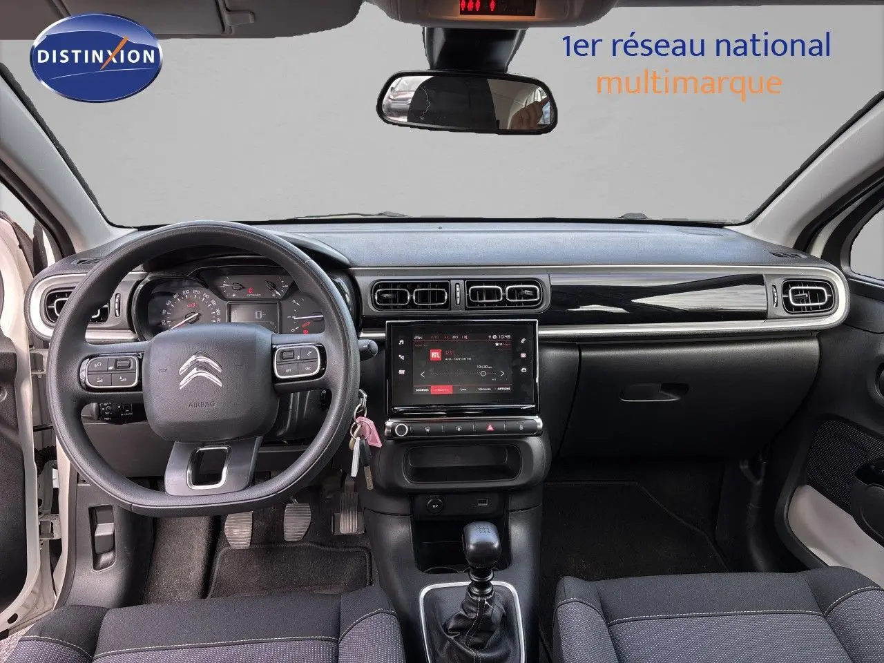 Vue intérieure avant du tableau de bord et volant d'une Citroën C3 blanc banquise 2022 avec boîte manuelle et écran tactile central.