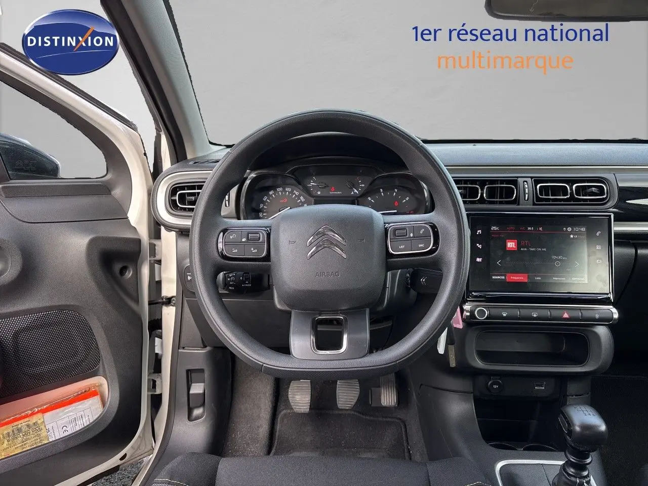 Vue intérieure centrée sur le volant et tableau de bord d'une Citroën C3 blanc banquise, avec écran tactile et portière ouverte côté gauche.