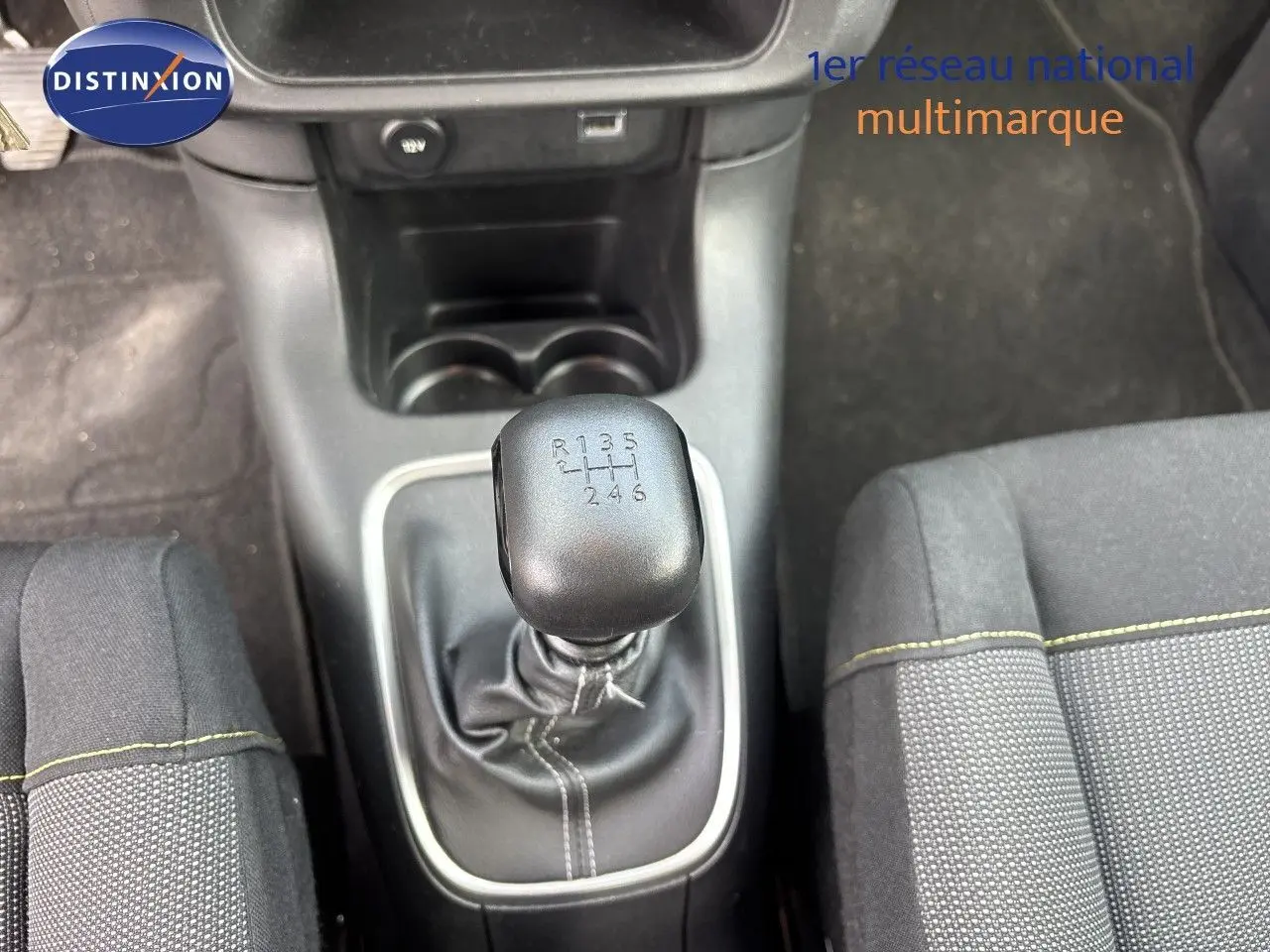 Vue rapprochée de la commande de boîte manuelle noire entourée de surpiqûres blanches dans l’habitacle du Citroën C3 blanc.