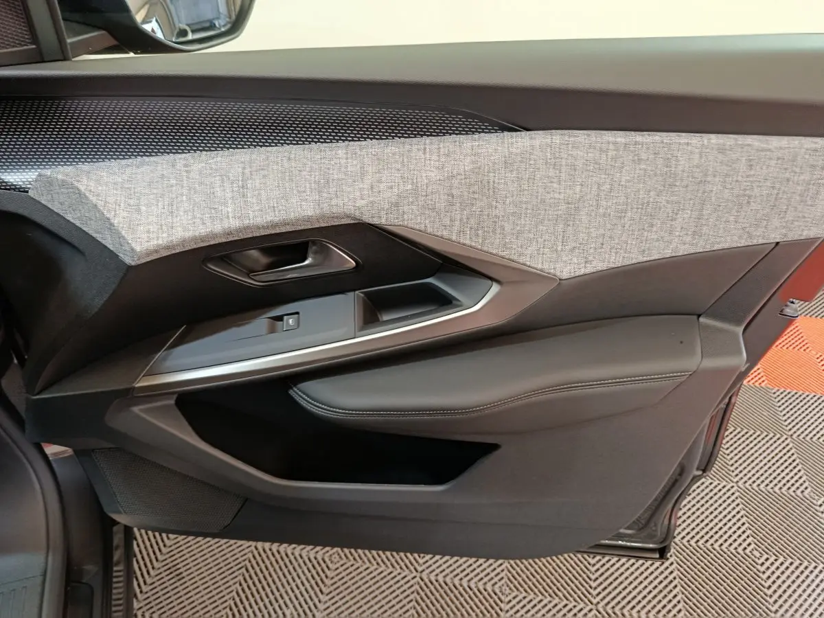 Vue intérieure côté gauche de la porte avant d’un Peugeot 3008 2025 avec habillage tissu gris et cuir noir.