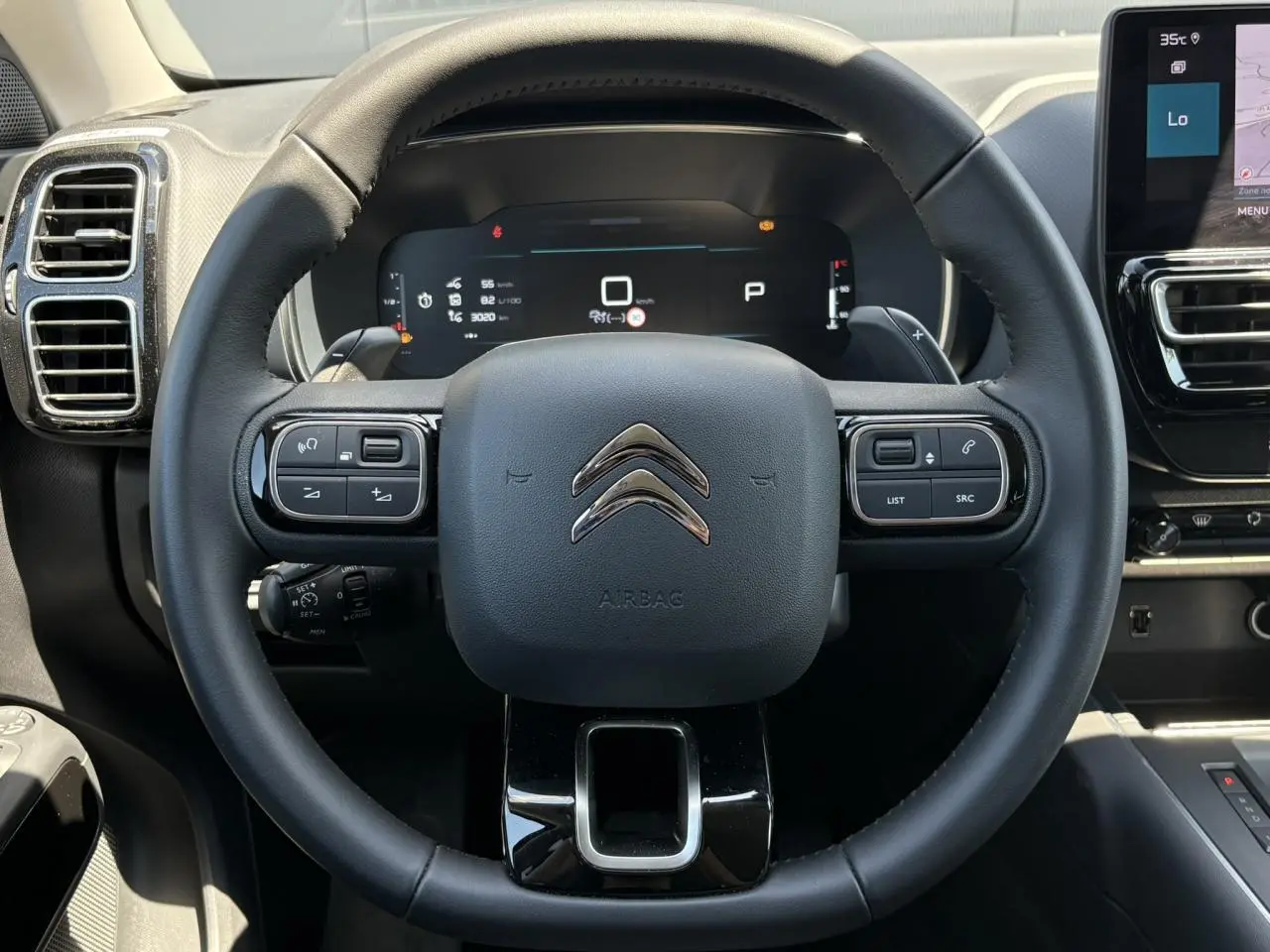 Vue frontale centrée sur le volant noir cuir du Citroën C5 Aircross Hybrid 2025 avec commandes intégrées et tableau de bord numérique.