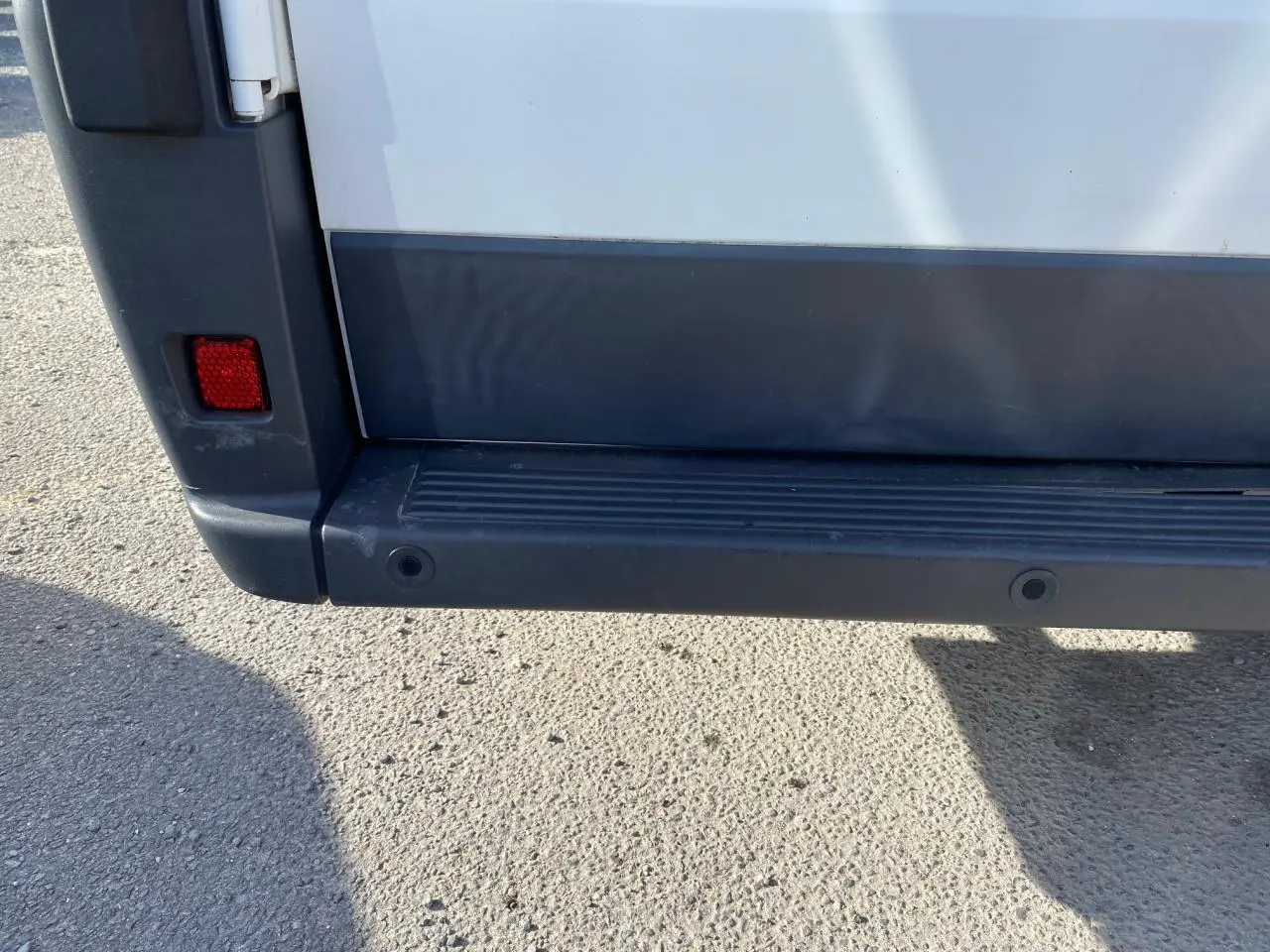 Gros plan sur le pare-chocs arrière noir et blanc du Citroën Jumper 2013 avec attelage visible en bas.